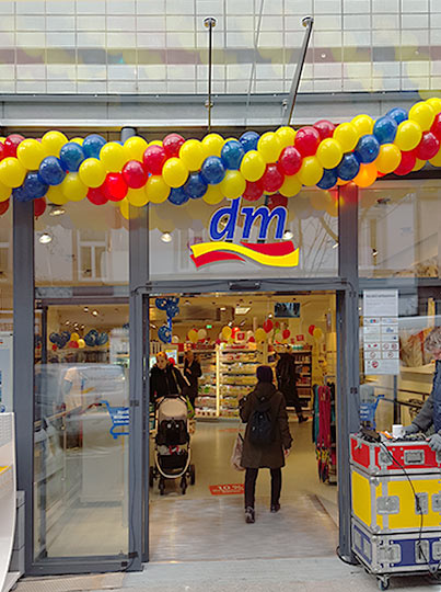 Der Eingangsbereich eines DM Drogeriemarktes in Frankfurt am Main. Luftballons säumen den Eingang. Das DM-Logo ist über der Tür angebracht.