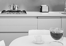 Die Küche für Ingenieure, Architekten, Verwalter, Projektentwickler bei vav. In der Mitte steht ein runder weißer Tisch. Im Hintergrund ist eine Küchenfront zu sehen. Ein Topf steht auf dem Herd. Oberhalb befinden sich Regale mit Geschirr. Links neben dem Herd steht eine Espresso-Maschine für schmackhaften Kaffee-Genuss.